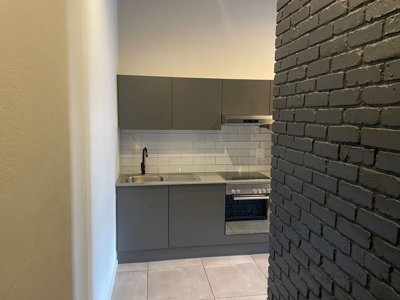 Modern compact kitchen featuring grey cabinetry, subway tile backsplash, integrated oven and hob, and a striking painted exposed brick feature wall.