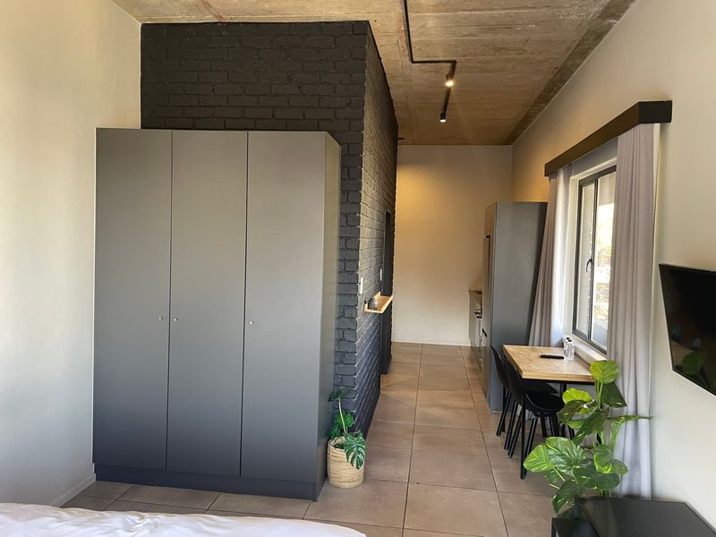 Modern open-plan apartment interior featuring an exposed concrete ceiling, industrial-style brick feature wall, tiled flooring, and integrated storage.