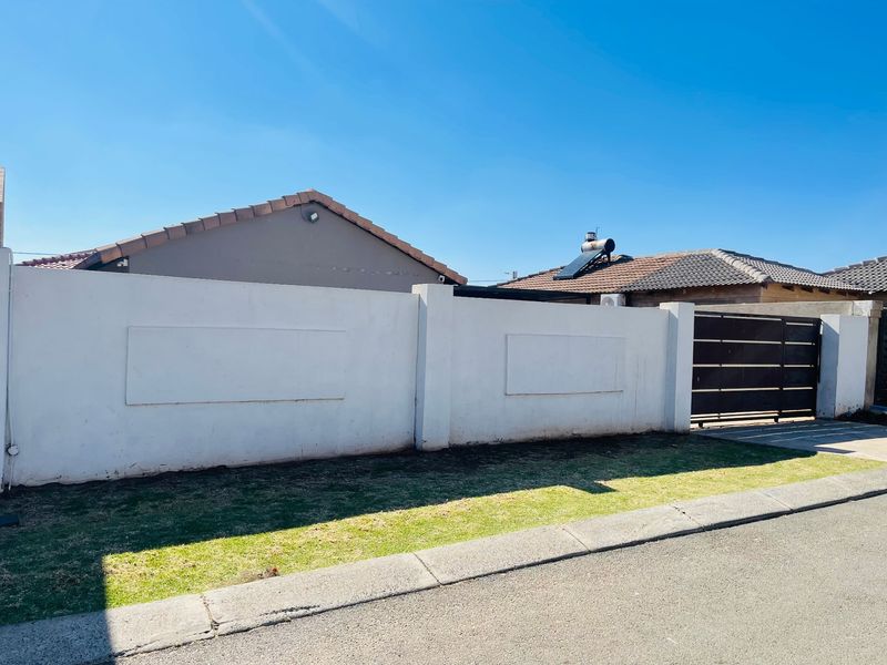 Front view of the property featuring a solid perimeter wall, metal driveway gate, and a tiled roof with a solar water heating system.