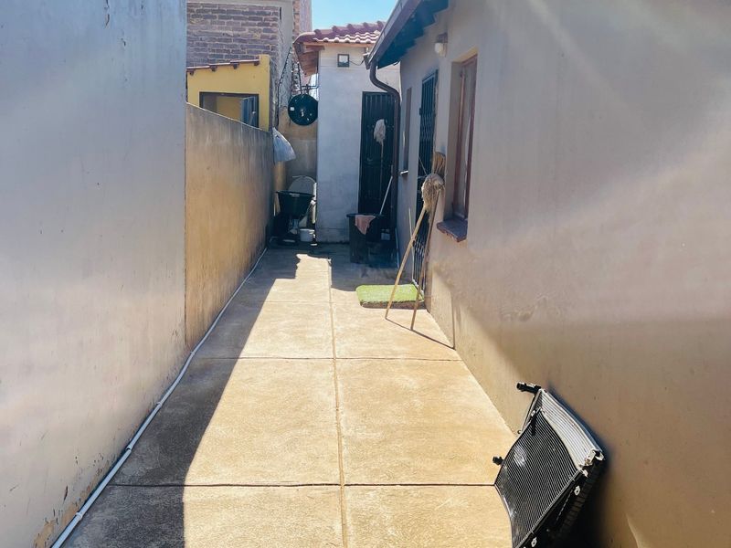 A narrow side passage or rear exterior walkway featuring concrete paving and boundary walls, providing access between building sections.