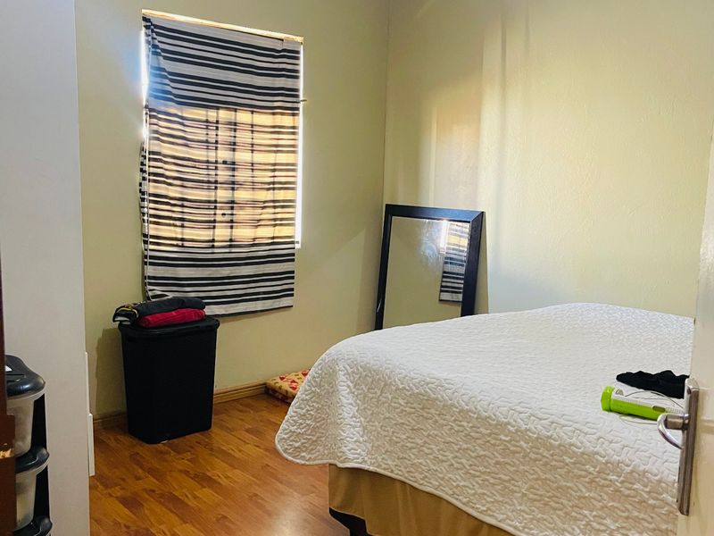 A standard bedroom featuring laminate flooring, neutral wall paint, and a window with a fitted blind.