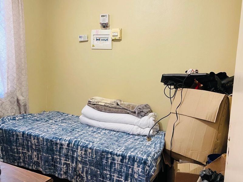 A bedroom featuring laminate flooring, coving, and wall-mounted electrical distribution and alarm control panels.
