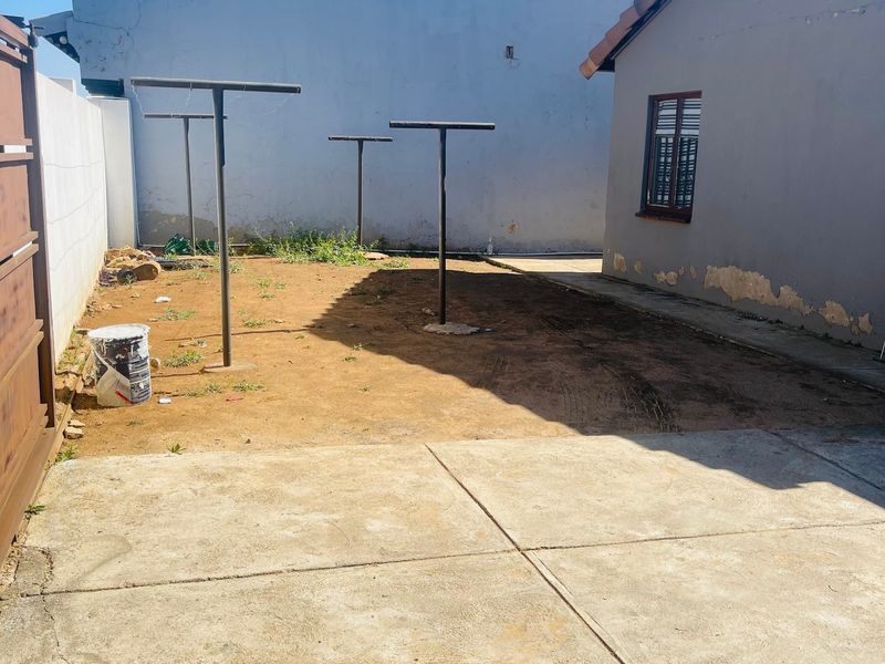 Rear exterior area featuring concrete paving, metal washing line poles, and a boundary wall, requiring landscaping and exterior wall maintenance.