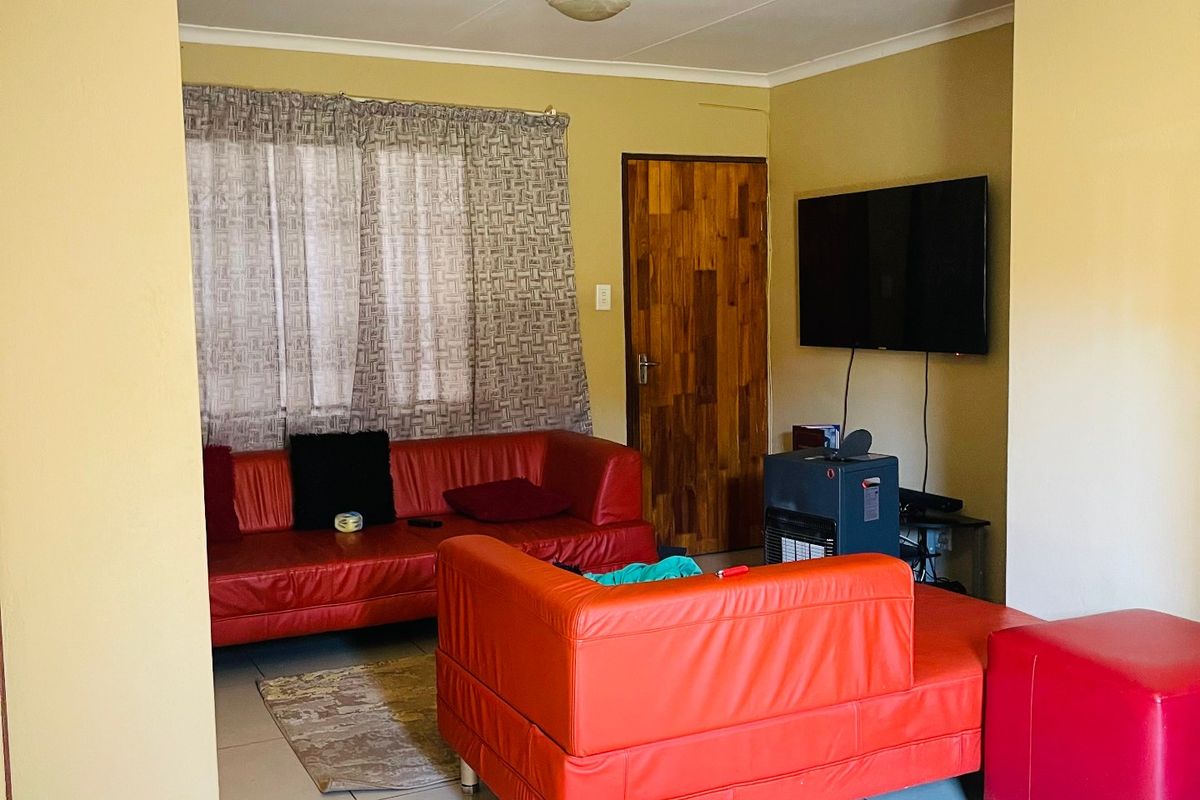 A living room featuring tiled flooring, cove cornicing, and a wooden door, providing a functional and neutral living space.