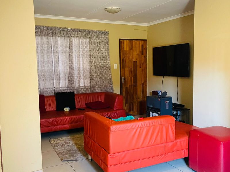 A living room featuring tiled flooring, cove cornicing, and a wooden door, providing a functional and neutral living space.