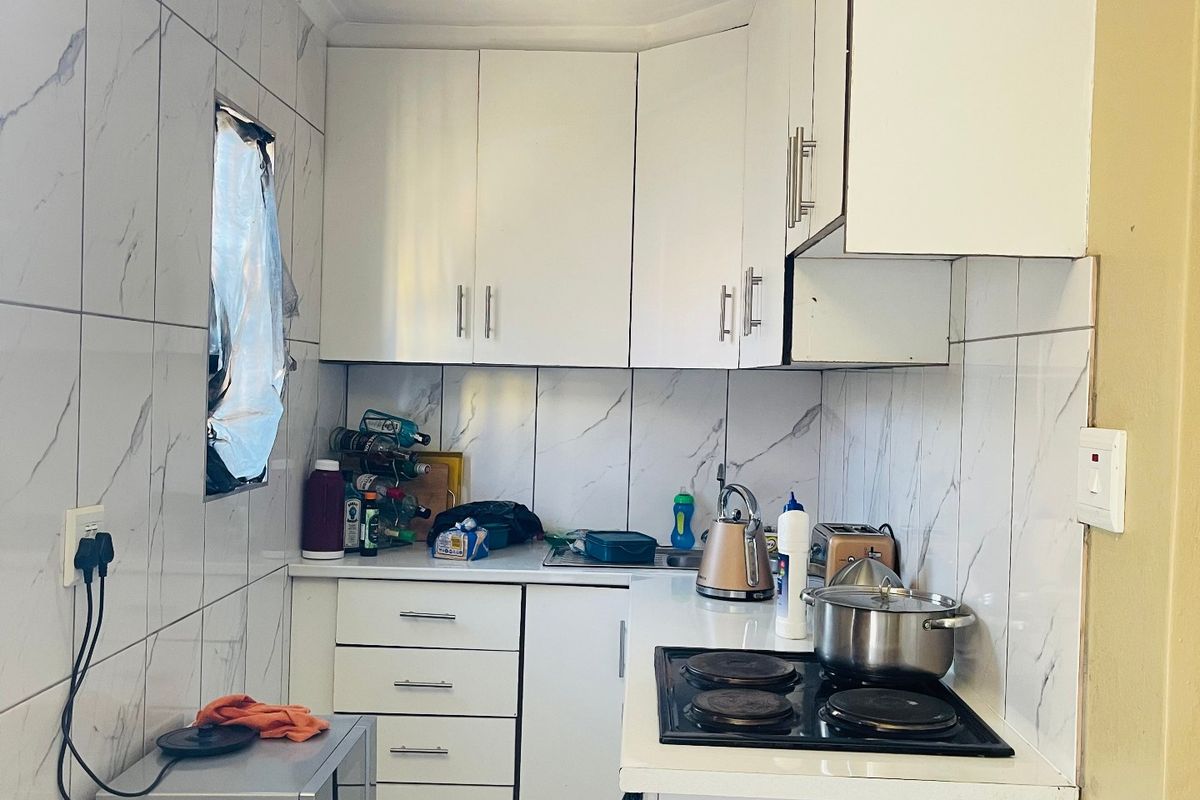 Compact kitchen featuring white cabinetry, marble-look wall tiles, and an integrated electric hob with oven.
