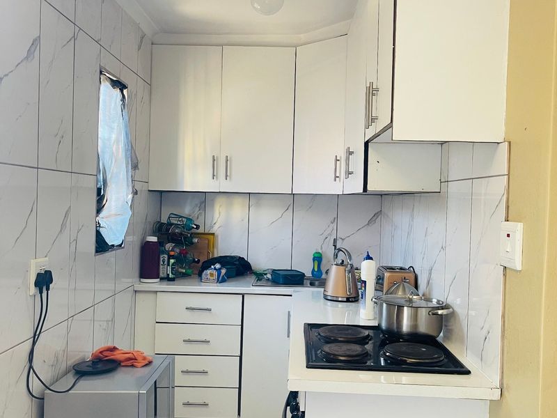 Compact kitchen featuring white cabinetry, marble-look wall tiles, and an integrated electric hob with oven.