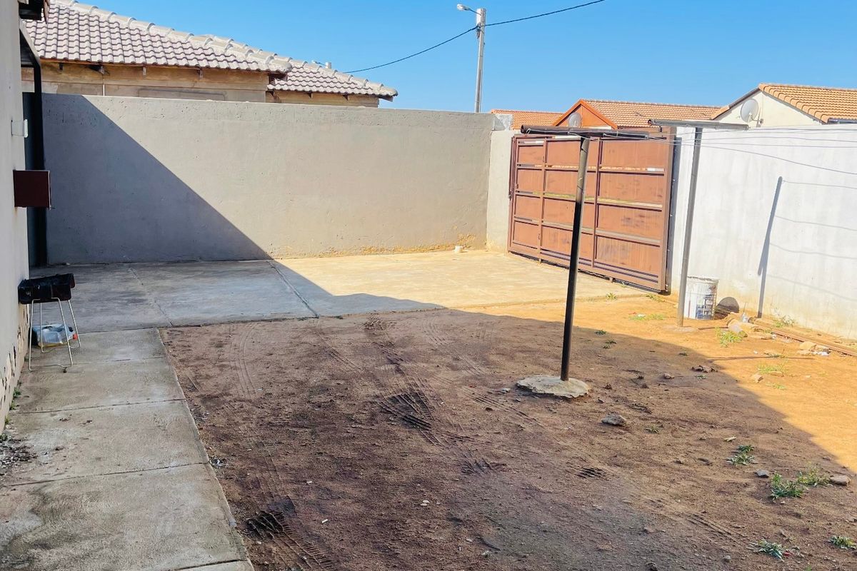 A rear exterior yard featuring concrete paving, a perimeter wall, and a metal gate, offering a blank canvas for landscaping or outdoor improvements.