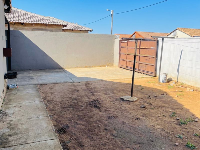 A rear exterior yard featuring concrete paving, a perimeter wall, and a metal gate, offering a blank canvas for landscaping or outdoor improvements.