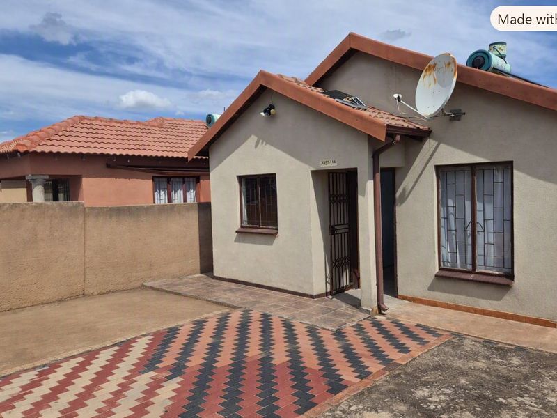 Front exterior view of a single-story house featuring a tiled roof, solar water heater, paved driveway, and secure entrance with burglar bars.