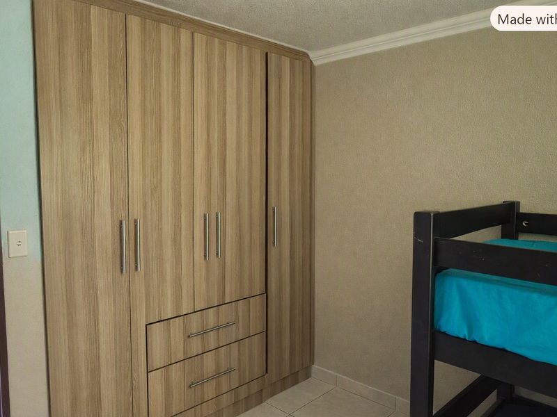 A bedroom featuring modern wood-finish built-in wardrobes with integrated drawers and tiled flooring.