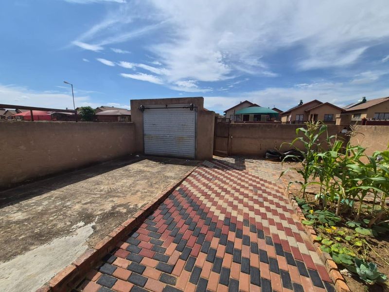Rear exterior area featuring a paved driveway, perimeter wall, and a roller garage door access point.