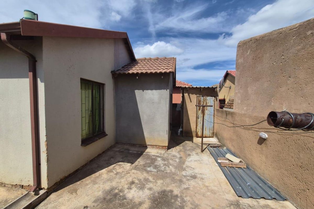 Rear exterior view of the property featuring a concrete patio area, boundary walls, and basic structural finishes requiring maintenance.