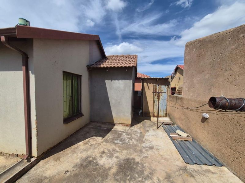Rear exterior view of the property featuring a concrete patio area, boundary walls, and basic structural finishes requiring maintenance.