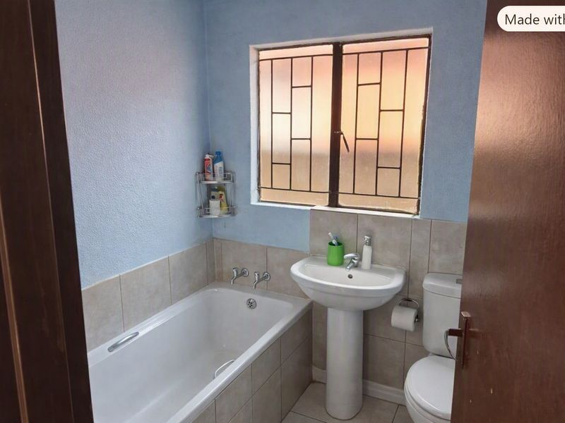A functional bathroom featuring a bathtub, pedestal basin, and toilet, with tiled splashbacks and a window fitted with security bars.