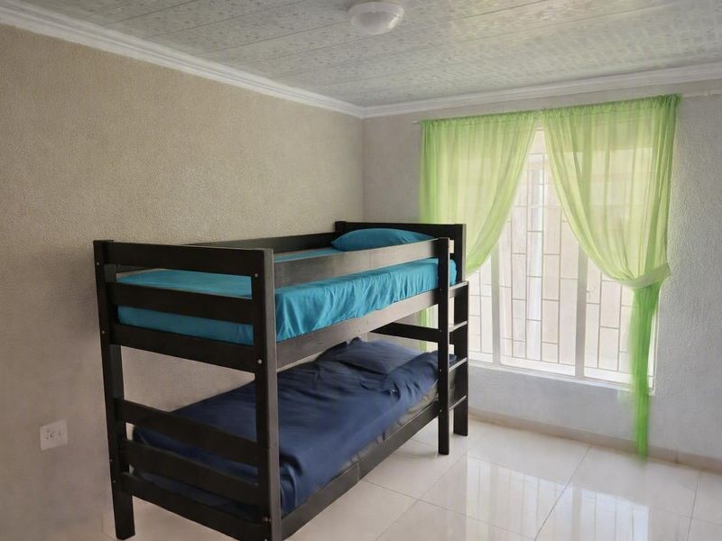 A bedroom featuring tiled flooring, textured walls, and a window fitted with security bars.