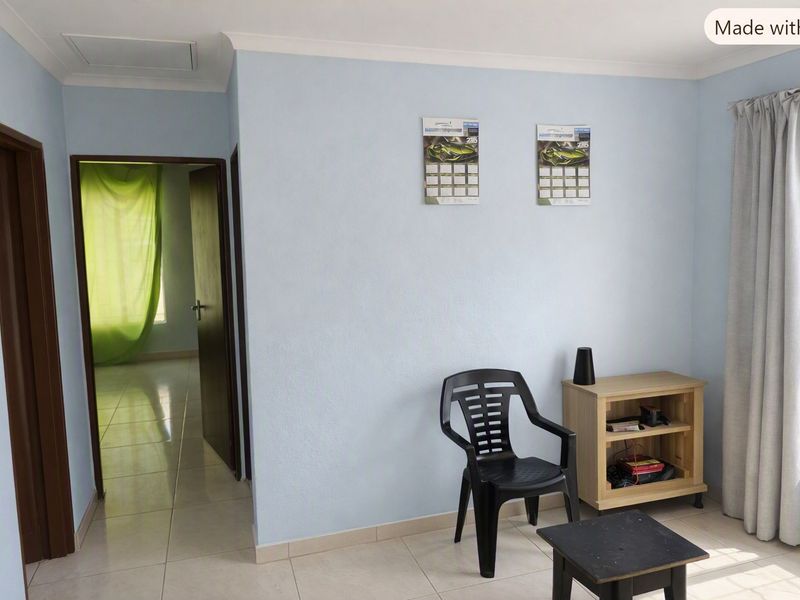A simple living area featuring light blue walls, tiled flooring, and a doorway leading to an adjacent room.