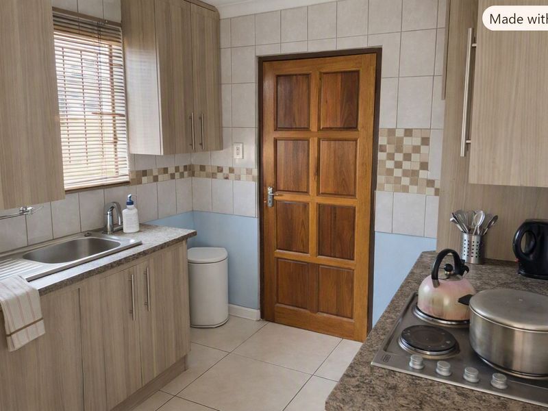 A functional kitchen featuring laminate cabinetry, stone-look countertops, a built-in hob, and tiled finishes, providing a practical workspace with direct access to an adjacent room.