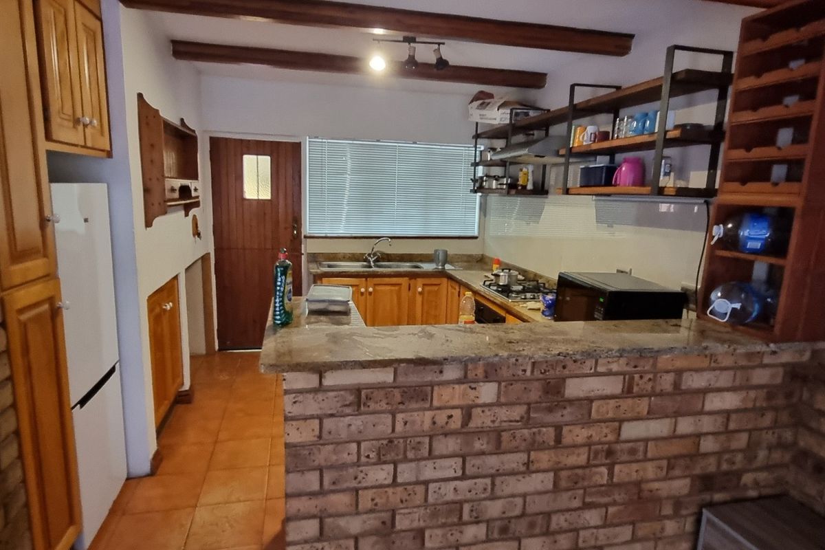 A rustic kitchen featuring exposed timber beams, brick walls, granite countertops, and wooden cabinetry, offering a warm, traditional aesthetic with functional layout.