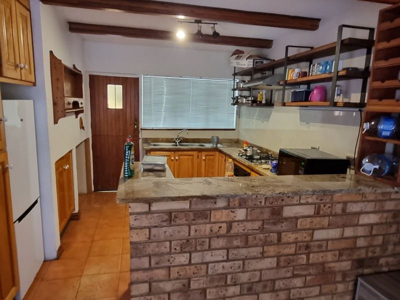 A rustic kitchen featuring exposed timber beams, brick walls, granite countertops, and wooden cabinetry, offering a warm, traditional aesthetic with functional layout.