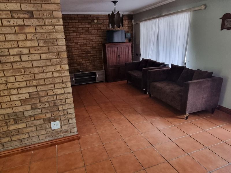 A living room featuring exposed brick walls, ceramic tile flooring, and access to an outdoor area through a security gate.