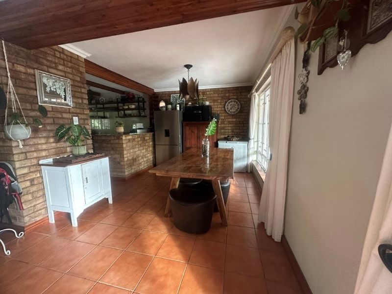 Open-plan dining and kitchen area featuring rustic face brick walls, exposed timber ceiling beams, and terracotta floor tiles.