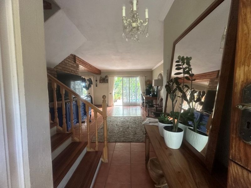 Open-plan living area featuring exposed brickwork, wooden ceiling beams, and a staircase, leading out to a patio through sliding glass doors.
