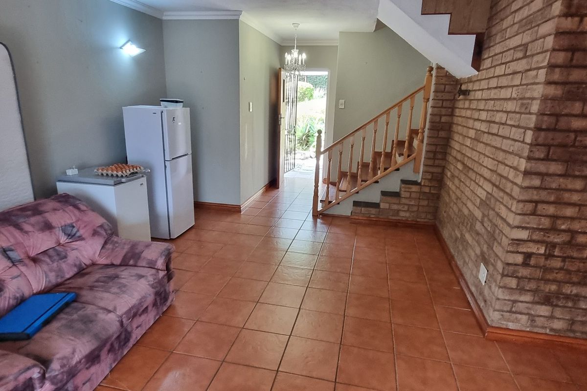 Living area featuring exposed brickwork, tiled flooring, and a wooden staircase leading to the upper level, with direct access to the entrance.