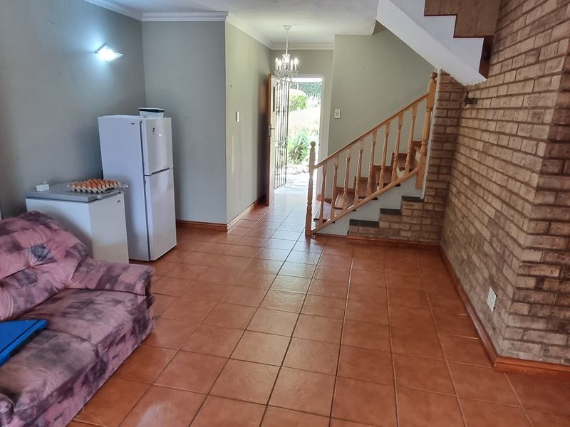 Living area featuring exposed brickwork, tiled flooring, and a wooden staircase leading to the upper level, with direct access to the entrance.