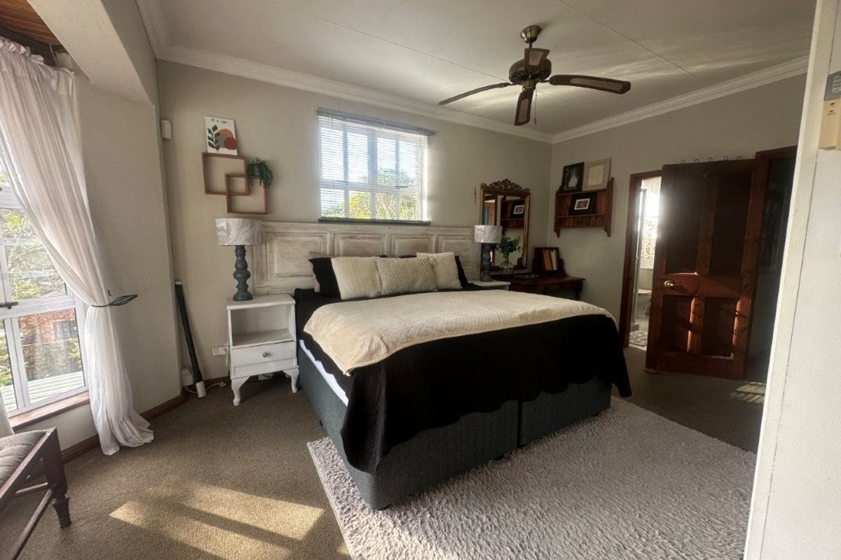 A spacious bedroom featuring neutral walls, crown molding, a ceiling fan, and carpeted flooring with direct access to an en-suite bathroom.