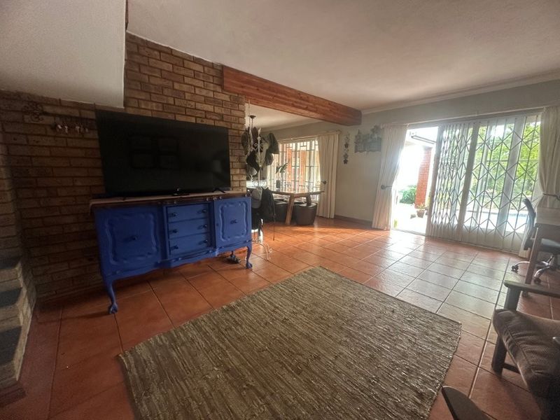 Spacious living room featuring exposed brick fireplace, timber ceiling beam, and terracotta floor tiles, with direct access to the outdoor area via sliding glass doors.