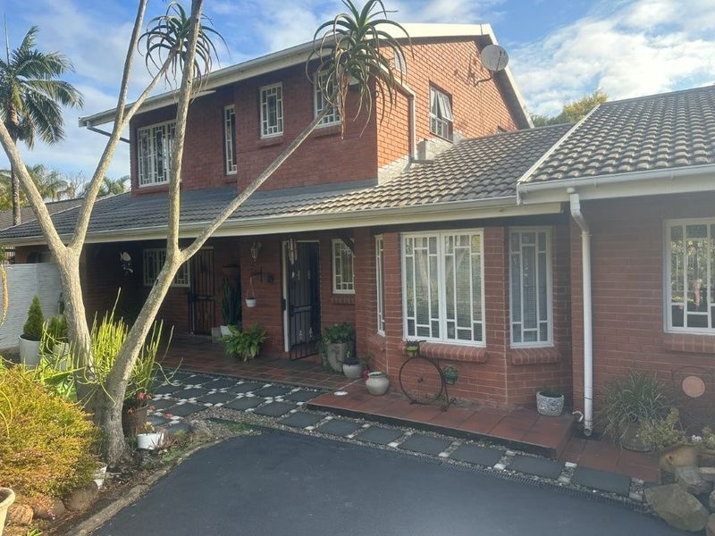 A well-maintained double-story brick house featuring a tiled roof, secure entrance, and a paved front walkway with established garden elements.