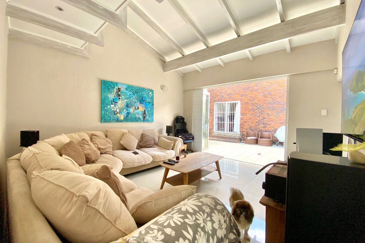 Spacious living room featuring high vaulted ceilings with exposed timber beams, polished tile flooring, and seamless access to an outdoor patio area.