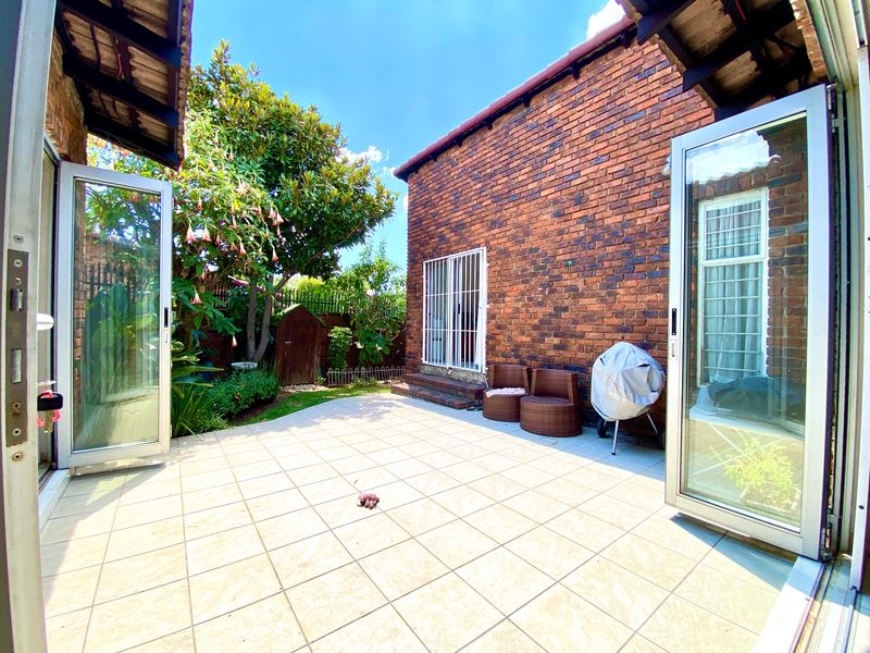 A private paved patio area featuring exposed brick walls, secure double glass doors, and direct access to a landscaped garden space.