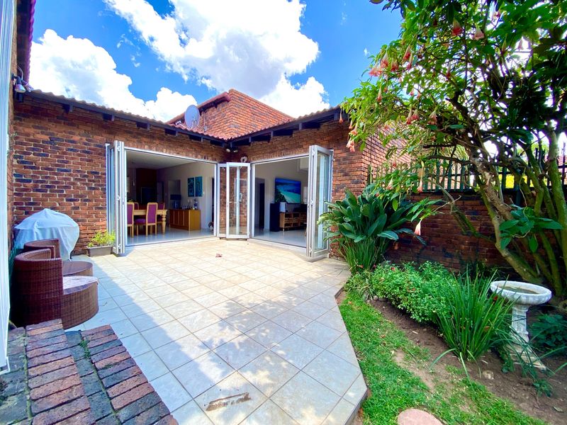 A well-maintained rear patio featuring tiled flooring and bi-fold doors that open into the living area, set against a face brick townhouse exterior.