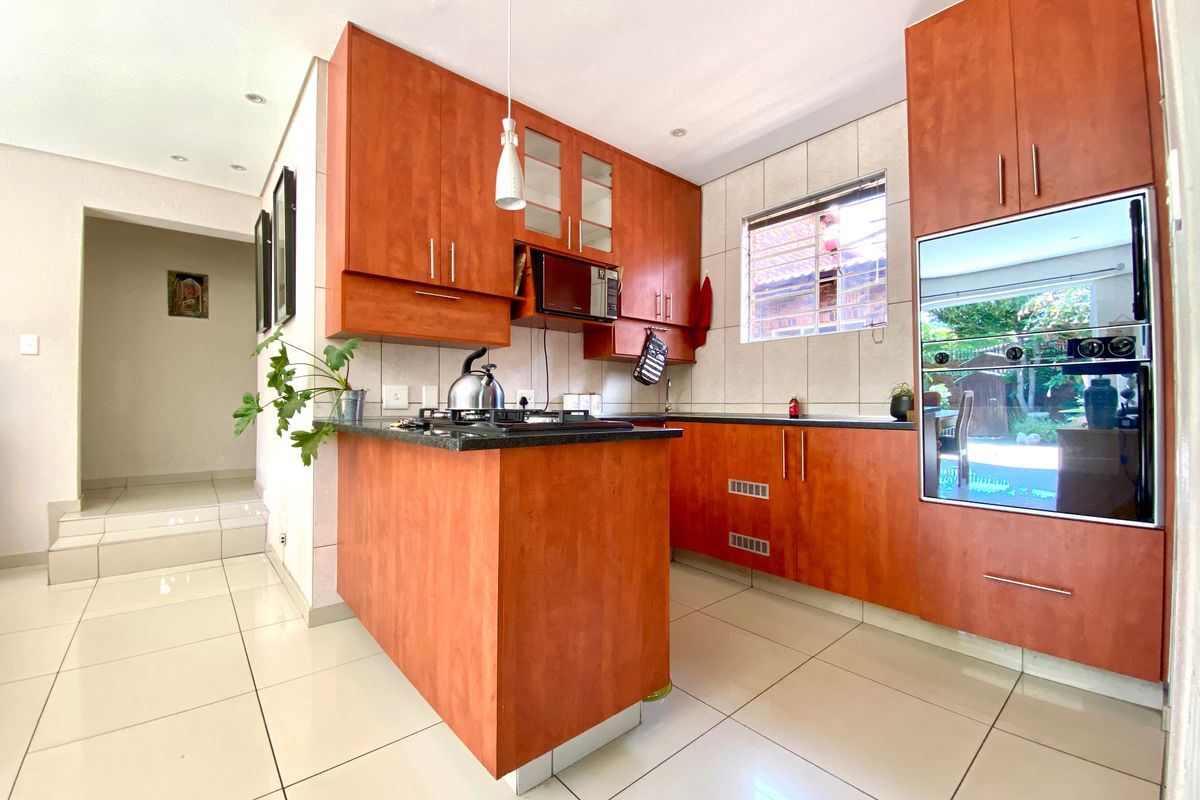 A functional kitchen featuring warm-toned wooden cabinetry, granite countertops, a gas hob, and integrated oven and microwave, complemented by neutral tiled flooring.