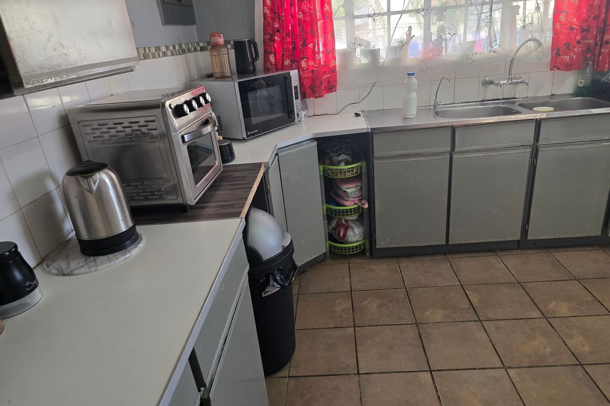 A functional kitchen featuring double bowl stainless steel sink, laminate countertops, tiled splashback, and original cabinetry with ceramic floor tiles.