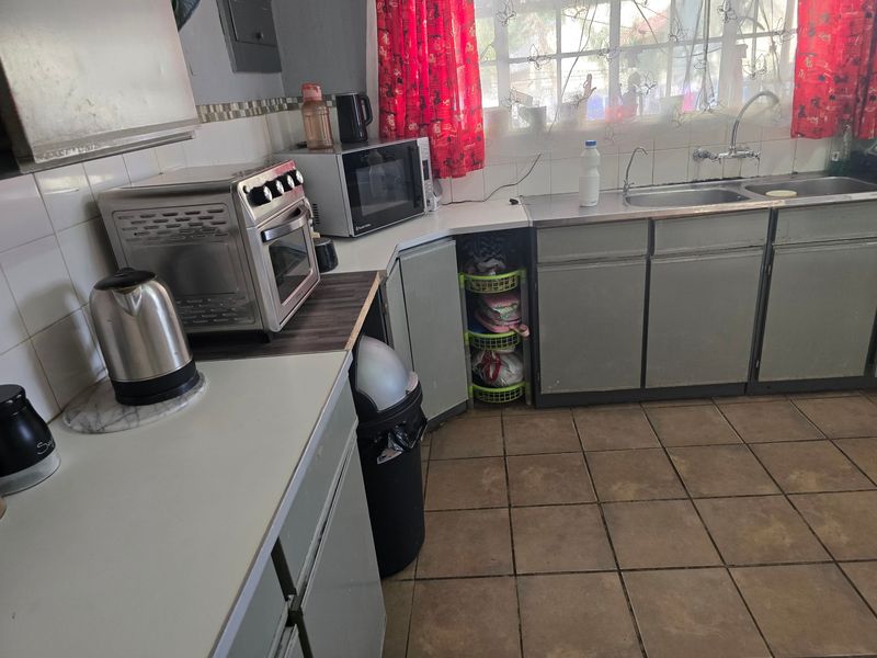 A functional kitchen featuring double bowl stainless steel sink, laminate countertops, tiled splashback, and original cabinetry with ceramic floor tiles.