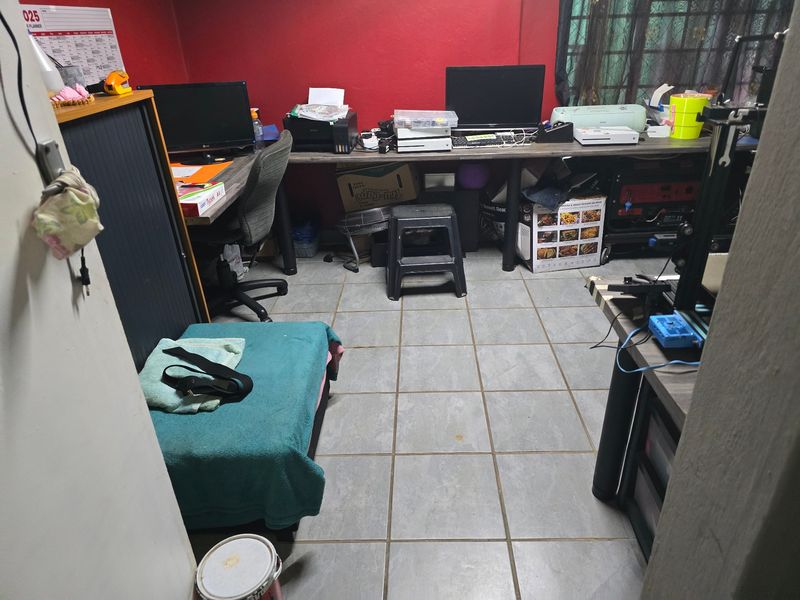 A functional home office space featuring tiled flooring and security bars on the window, currently utilized as a workspace.
