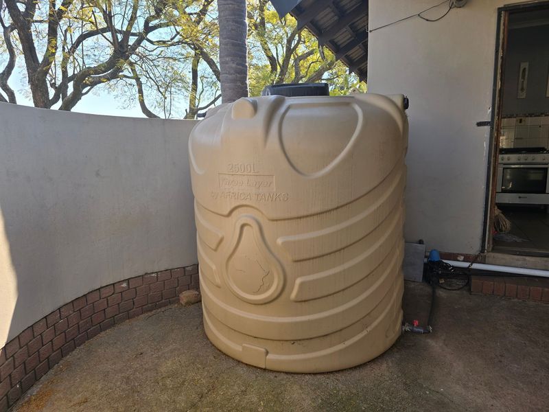 Exterior utility area featuring a 2500L water storage tank with an integrated pump system, situated on a concrete paved surface.