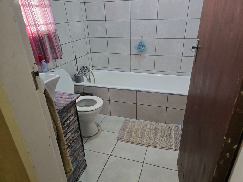 A functional bathroom featuring a bathtub, toilet, and vanity cabinet with tiled walls and flooring throughout.