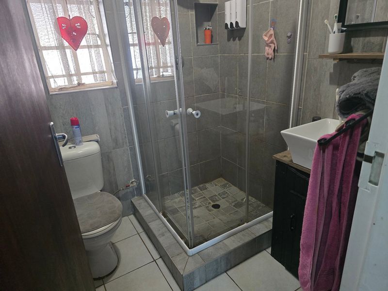 Compact bathroom featuring a tiled shower enclosure, modern vessel sink with vanity cabinet, and neutral wall tiling.