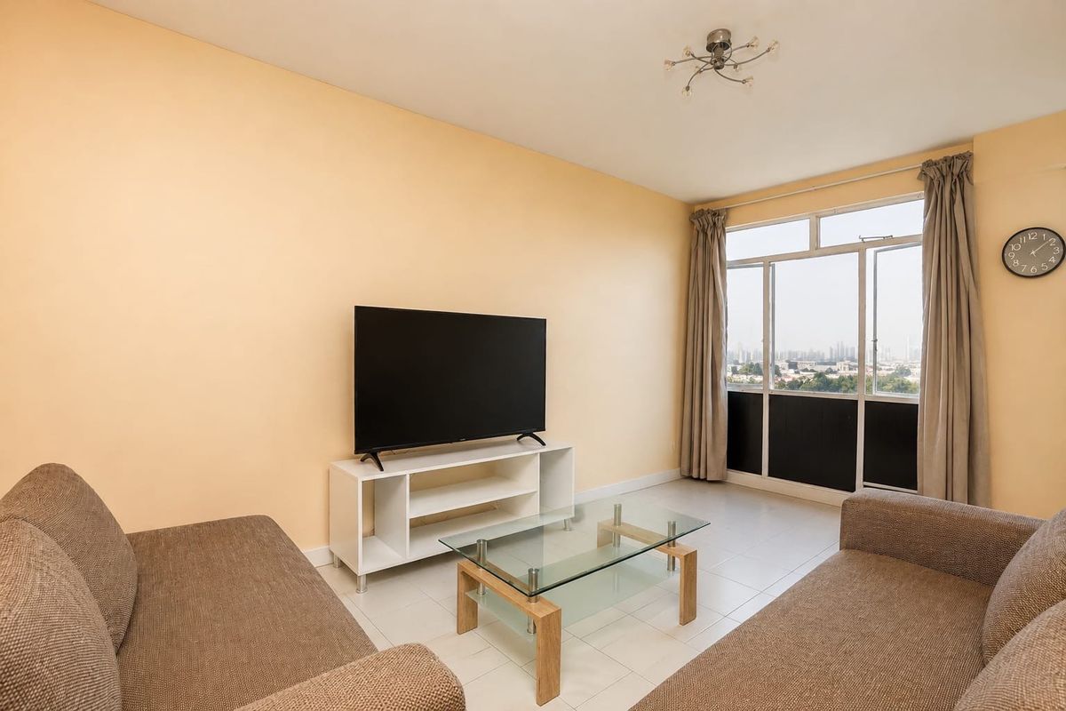 A bright living room featuring tiled flooring and a large window with natural light, offering a view of the surrounding area.