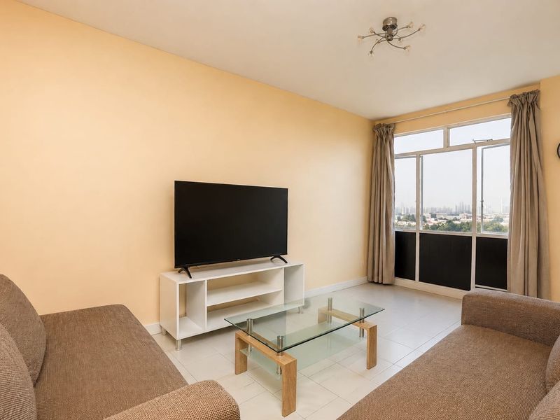 A bright living room featuring tiled flooring and a large window with natural light, offering a view of the surrounding area.