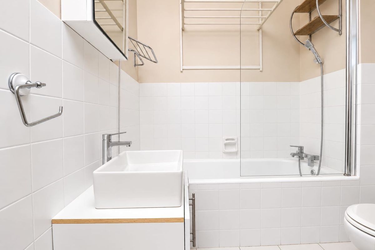 A clean, modern bathroom featuring a white vessel sink, vanity cabinet, bathtub with a glass shower screen, and wall-mounted shower fixtures.