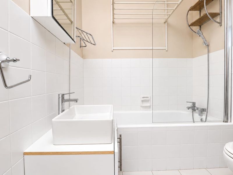 A clean, modern bathroom featuring a white vessel sink, vanity cabinet, bathtub with a glass shower screen, and wall-mounted shower fixtures.