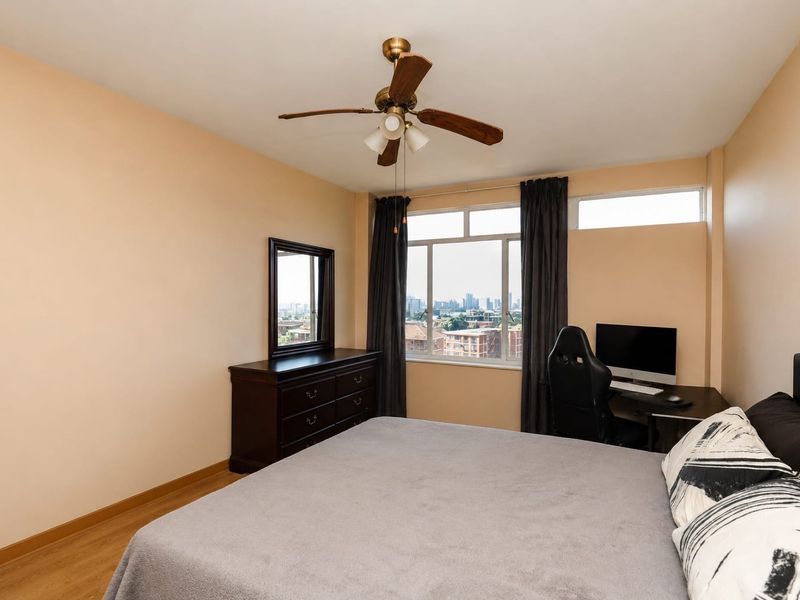 A bedroom featuring laminate flooring, a ceiling fan, and large windows providing natural light and city views.