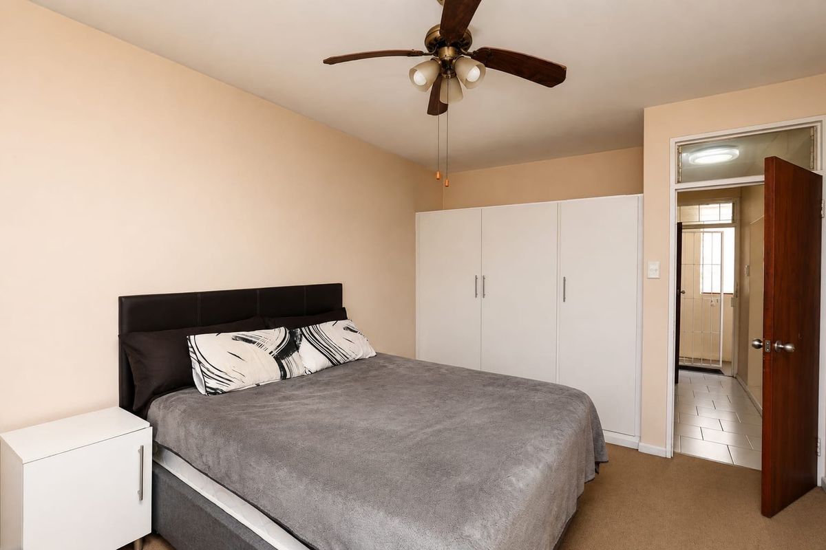 A bedroom featuring a ceiling fan and built-in white wardrobes, with an open doorway leading to an adjacent tiled area.