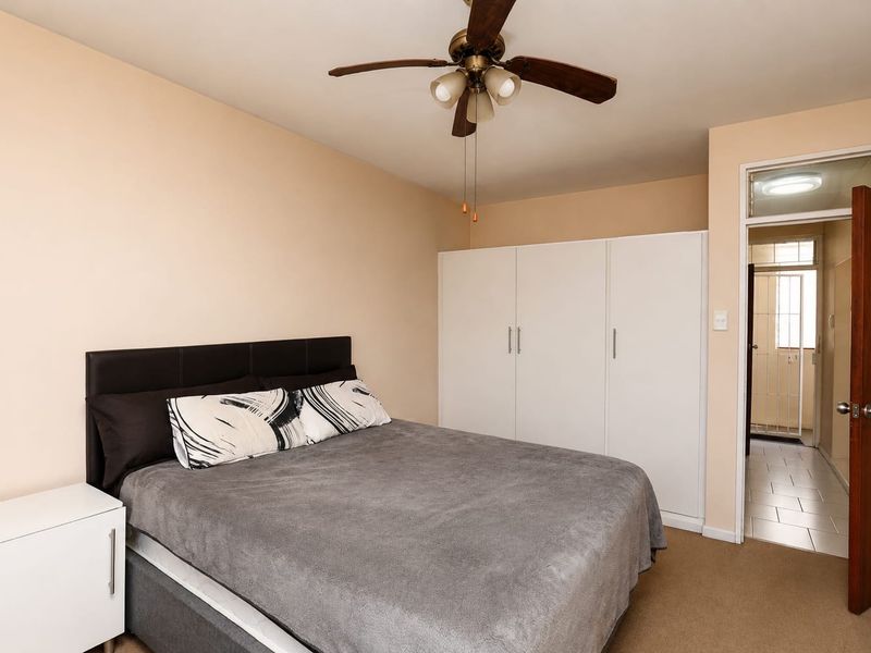 A bedroom featuring a ceiling fan and built-in white wardrobes, with an open doorway leading to an adjacent tiled area.