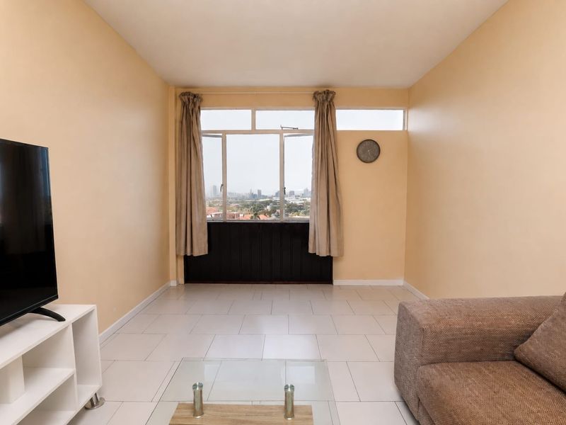 A living room featuring tiled flooring and large windows with city views, offering a bright and functional space.